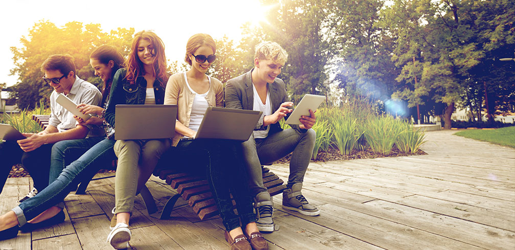 Junge Menschen sitzen zusammen auf einer Bank und halten Laptops und Tablets